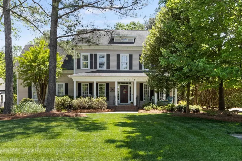 White colonial home framed by tall trees and green lawn