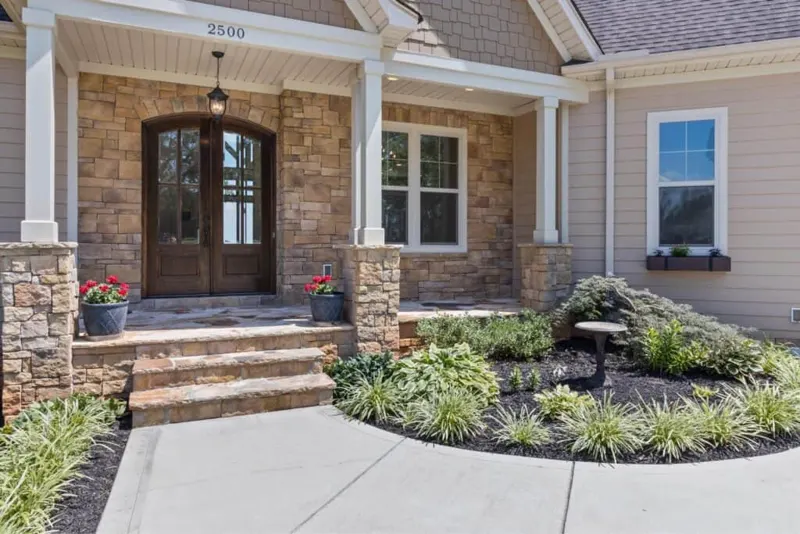 Stone front porch with double wooden doors and landscaping