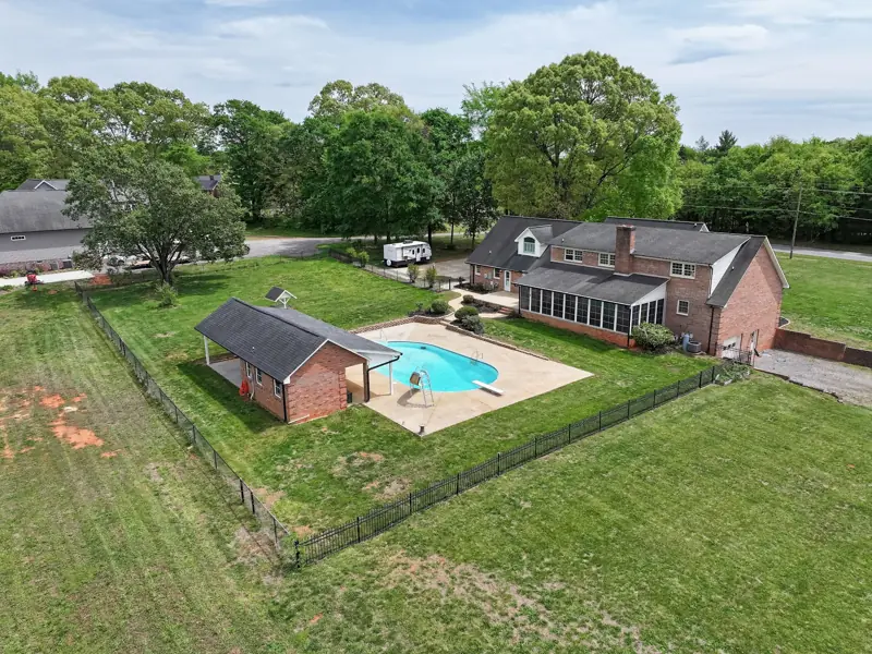 Drone view of a brick ranch with pool and fenced yard