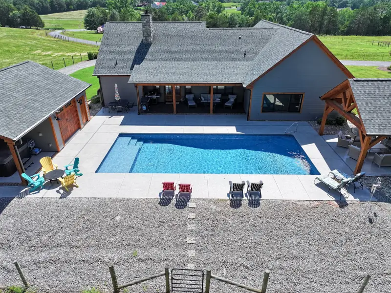 Aerial view of a gray home with a rectangular pool and timber pavilion