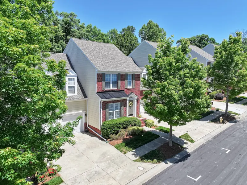Drone view of a brick townhome on a wooded street