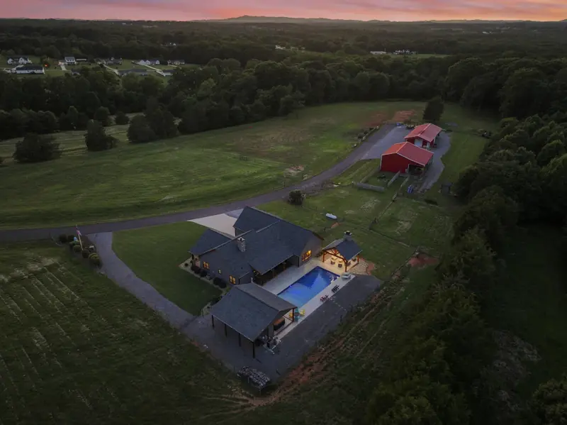 Drone view at dusk of a home on acreage with a lit pool