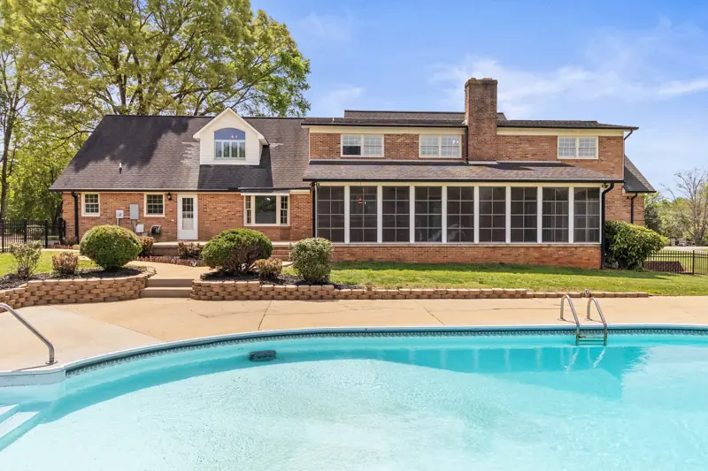 Backyard pool in front of a brick home with screened porch