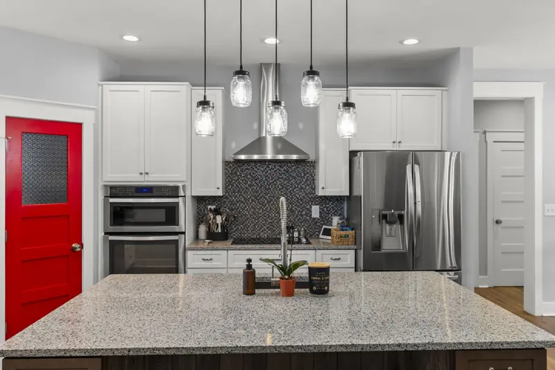 White kitchen with stone island, pendant lights and red pantry door