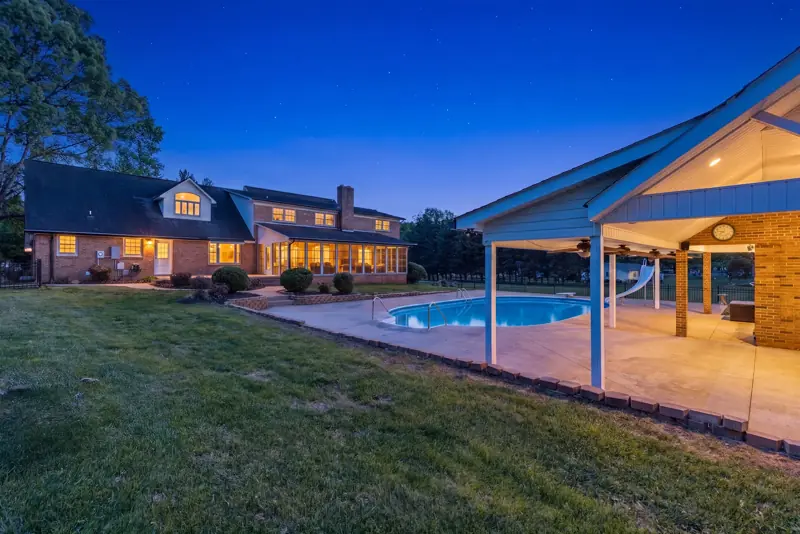 Covered patio and pool at dusk with lit home in background