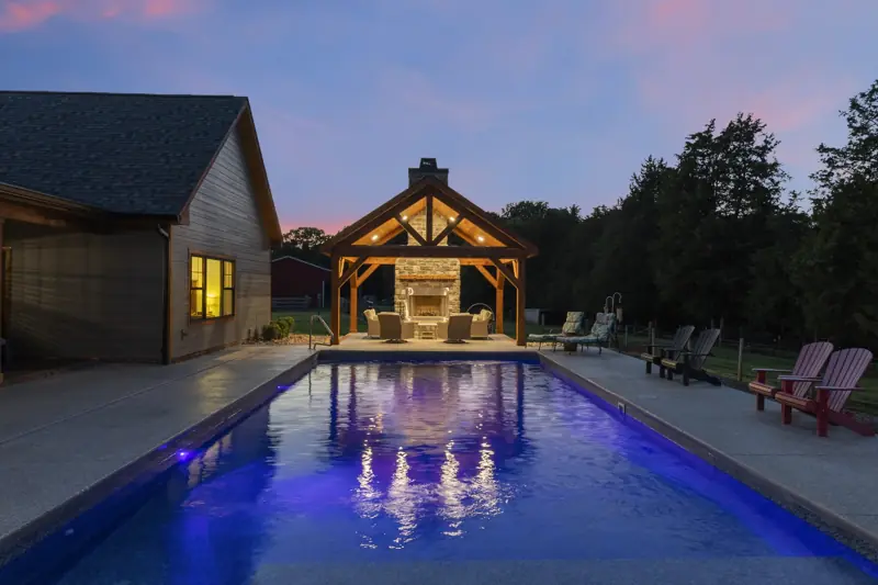 Lit pool and outdoor fireplace pavilion at twilight
